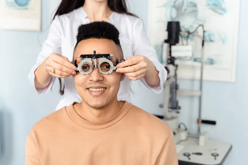 Optometrista coloca uma armação de prova a um paciente sorridente durante o exame à vista