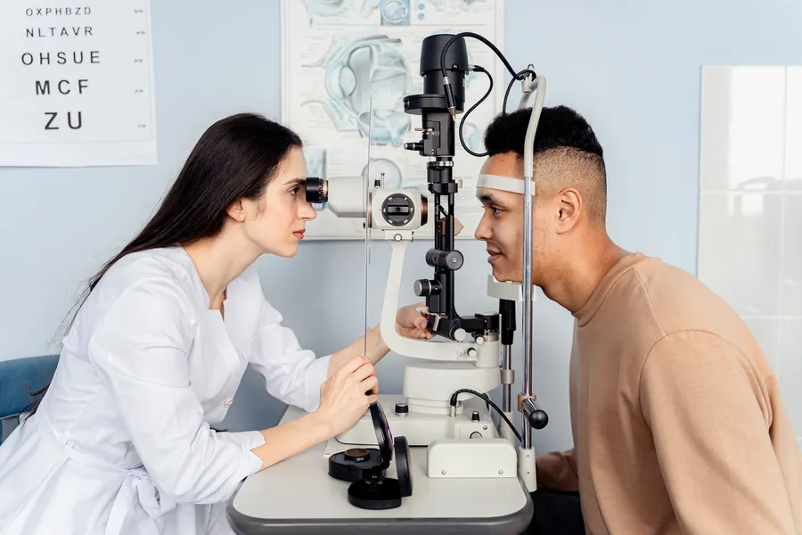 Optometrista observa o olho de um paciente numa lâmpada de fenda durante a consulta